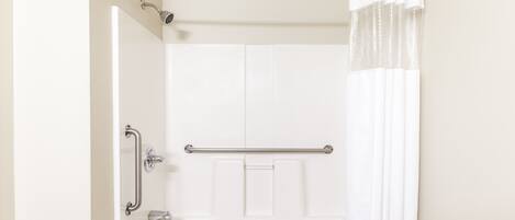 Une salle de bain avec une baignoire blanche, une douche dotée d’une porte en verre et une barre d’appui.