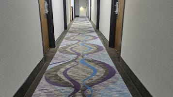 A hotel hallway with a patterned carpet, doors on both sides, and a light at the end.
