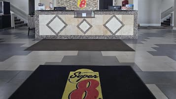 Zona de recepción de un hotel con el logotipo de Super 8 en el felpudo, un mostrador de recepción y una escalera al fondo.