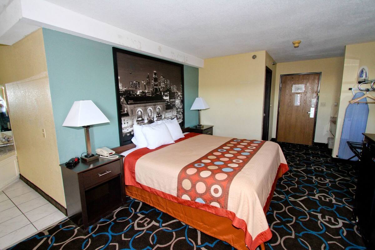Habitación de hotel con cama, dos mesitas de noche, un espejo, televisor montado en la pared y una puerta.