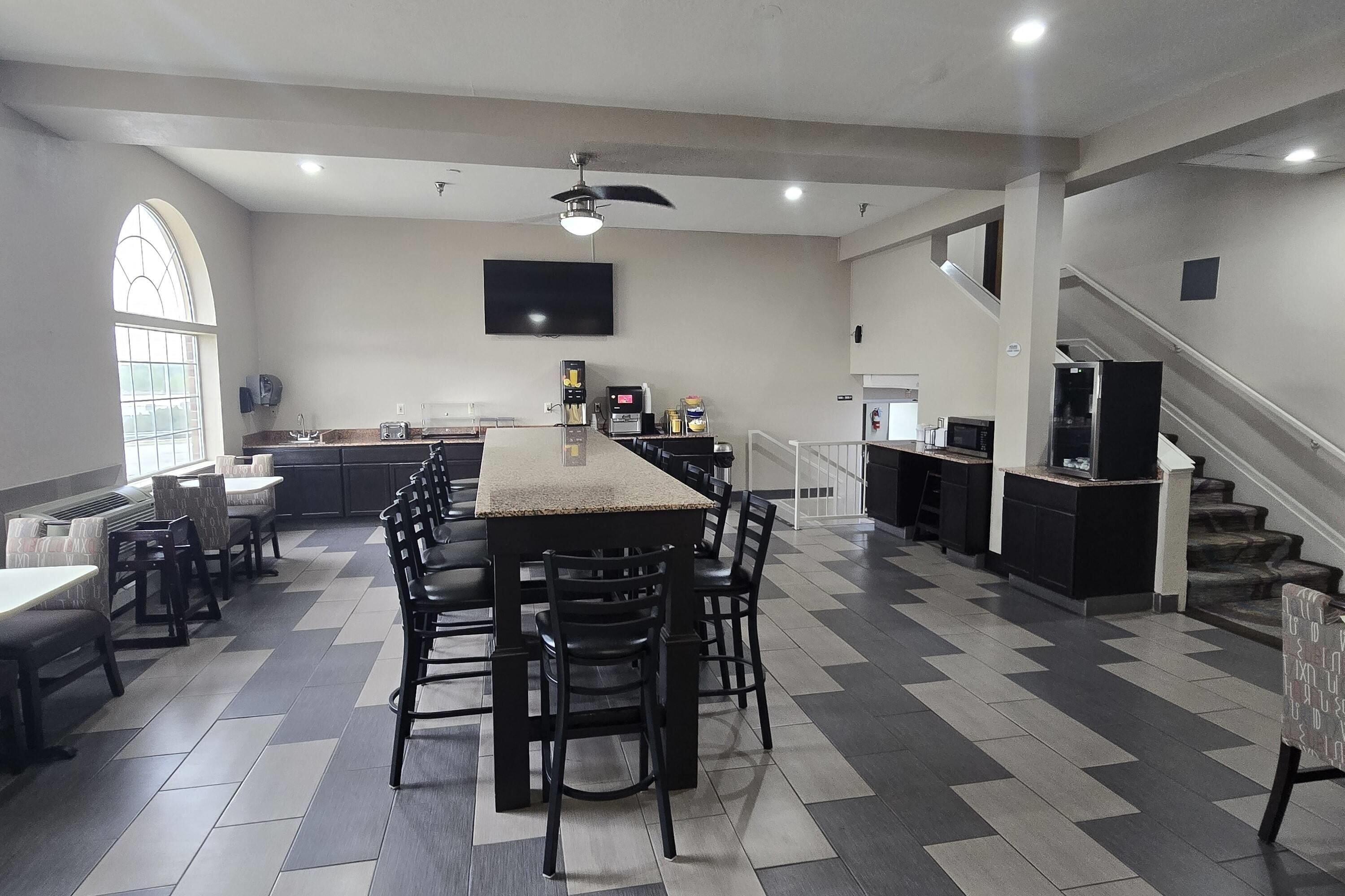 A spacious kitchen with a central island, dining area with chairs, a large window, and a staircase.