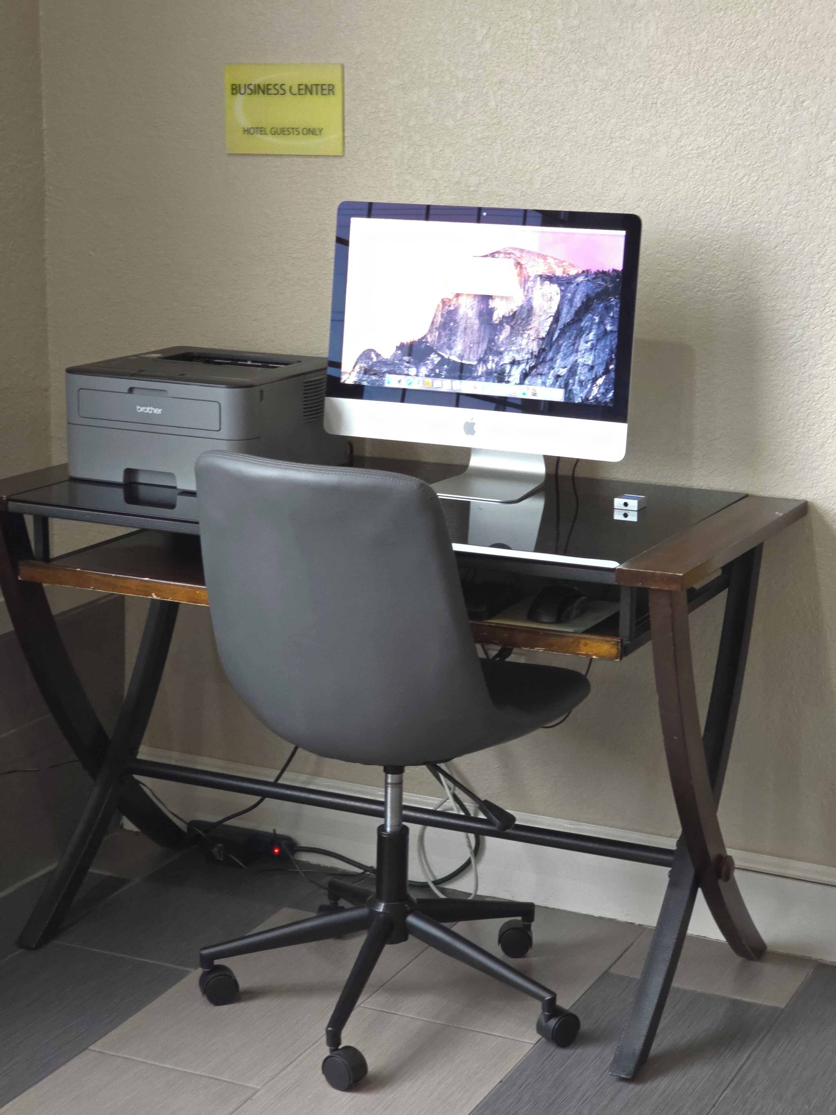 Escritorio con monitor, impresora y silla en una habitación de hotel.