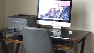 A computer desk with a monitor, printer, and chair in a hotel room.