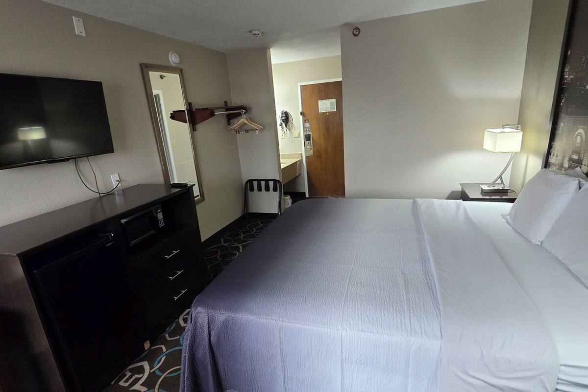 Habitación de hotel con cama, televisor, cómoda, espejo y puerta que da a un baño.