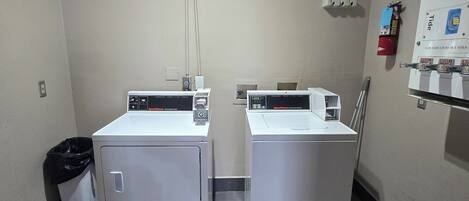 A laundry room with two front-loading washing machines and a dryer, a trash bin, and a fire extinguisher on the wall.