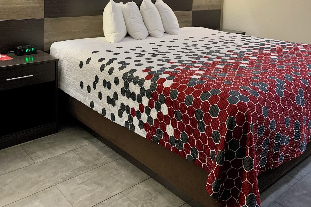 A hotel room with a bed, nightstands, a wall-mounted clock, and a wall-mounted light fixture.