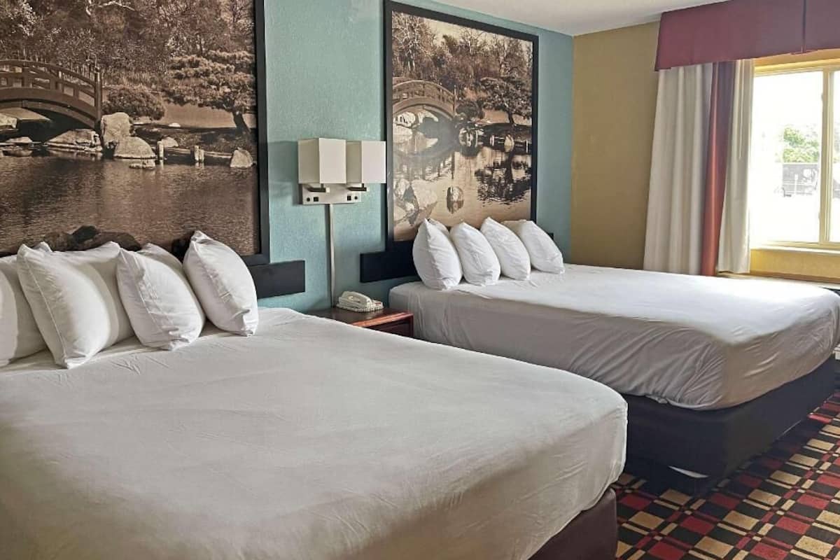 A hotel room with two beds, a large wall mural, a telephone, and a window with curtains.