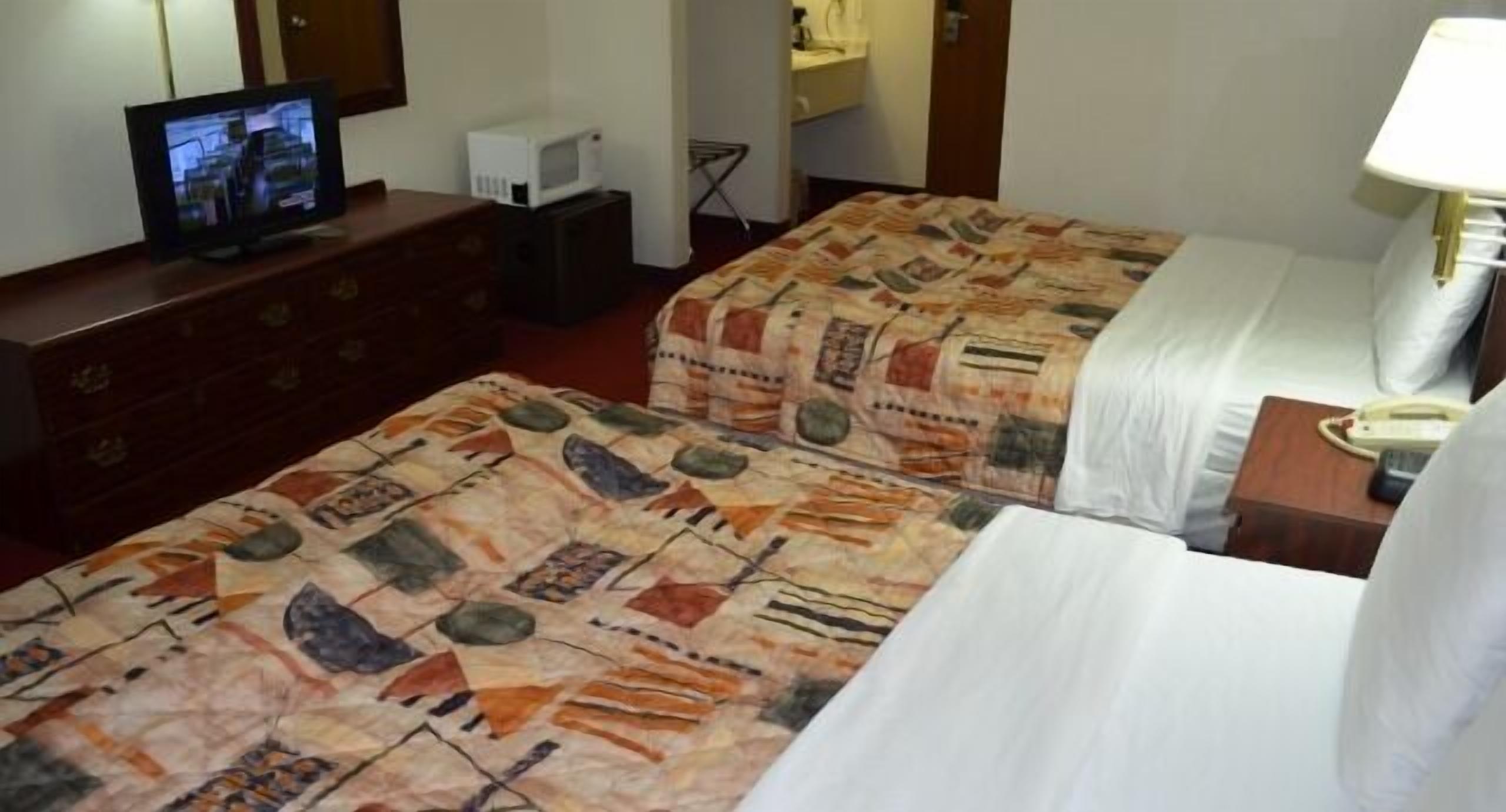 A hotel room with two beds, a television on a dresser, a microwave, and a telephone on a nightstand.