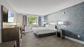 A modern hotel room with a large bed, a desk, a TV, and a window with curtains.