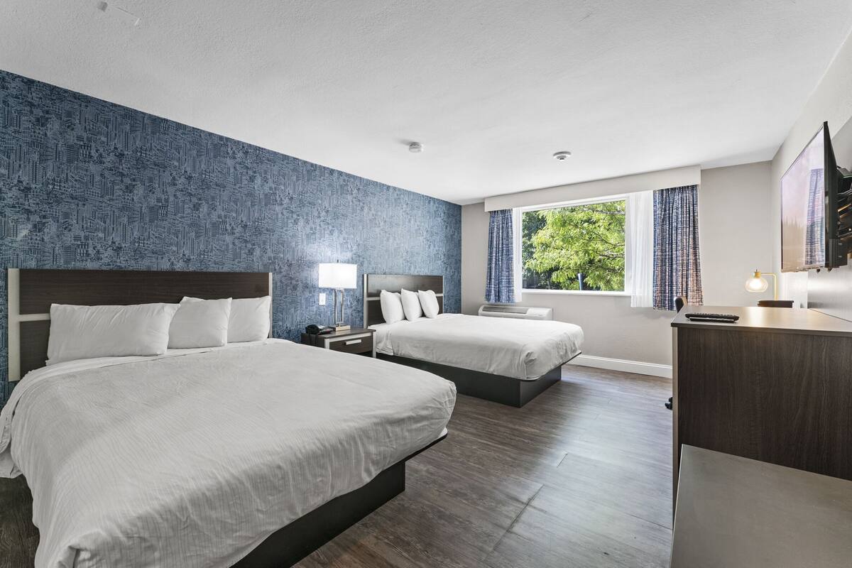 A hotel room with two beds, a desk, a TV, and a window with curtains.