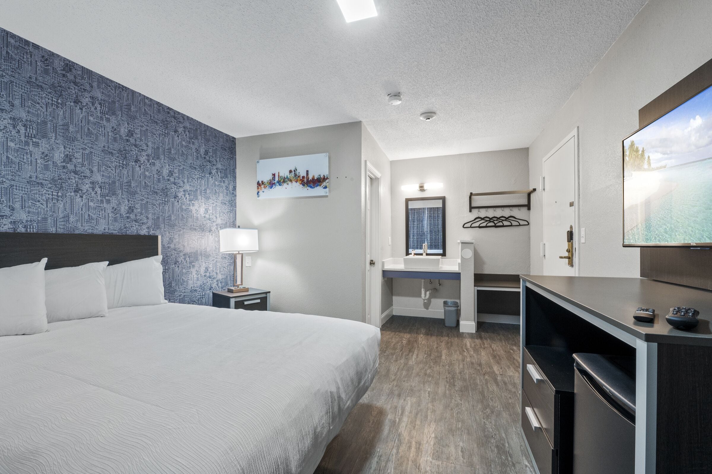 A hotel room with a large bed, a desk with a computer, a TV, and a bathroom with a shower and toilet.