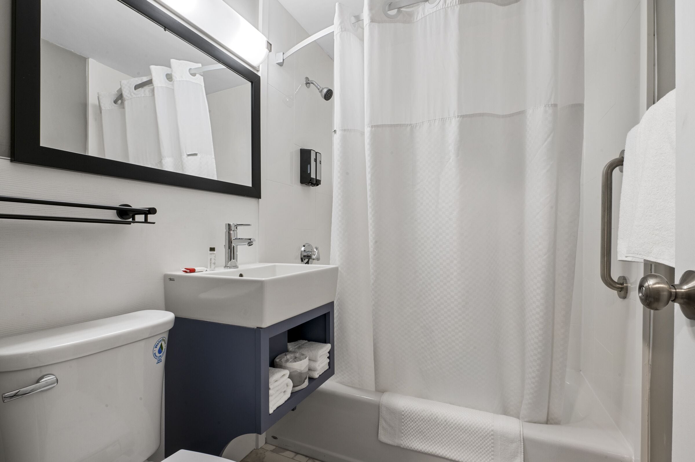Un baño con lavamanos blanco, espejo, inodoro y zona de ducha con cortina.