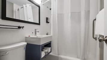 Un baño con lavamanos blanco, espejo, inodoro y zona de ducha con cortina.