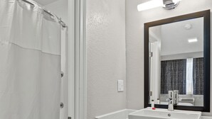 A bathroom with a white sink, mirror, and shower curtain. - The Inn on Arsenal (Watertown)