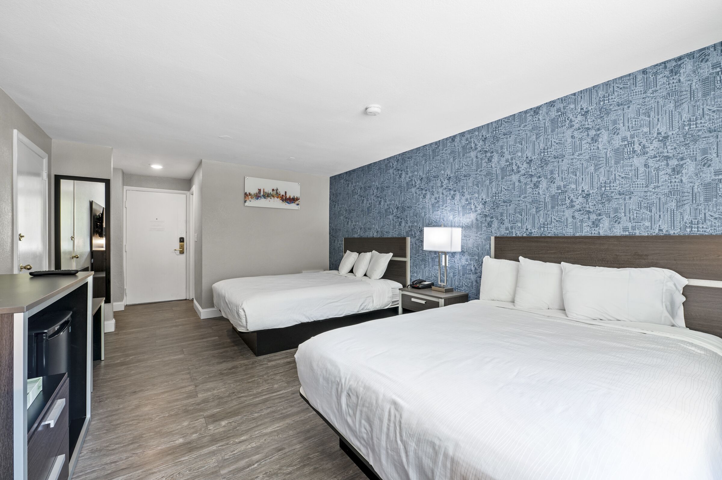 A hotel room with two beds, a desk, and a mirror.