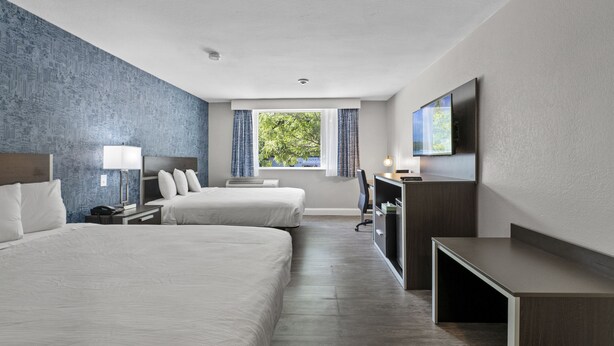 A hotel room with two beds, a desk, a TV, and a window with curtains. - The Inn on Arsenal (Watertown)