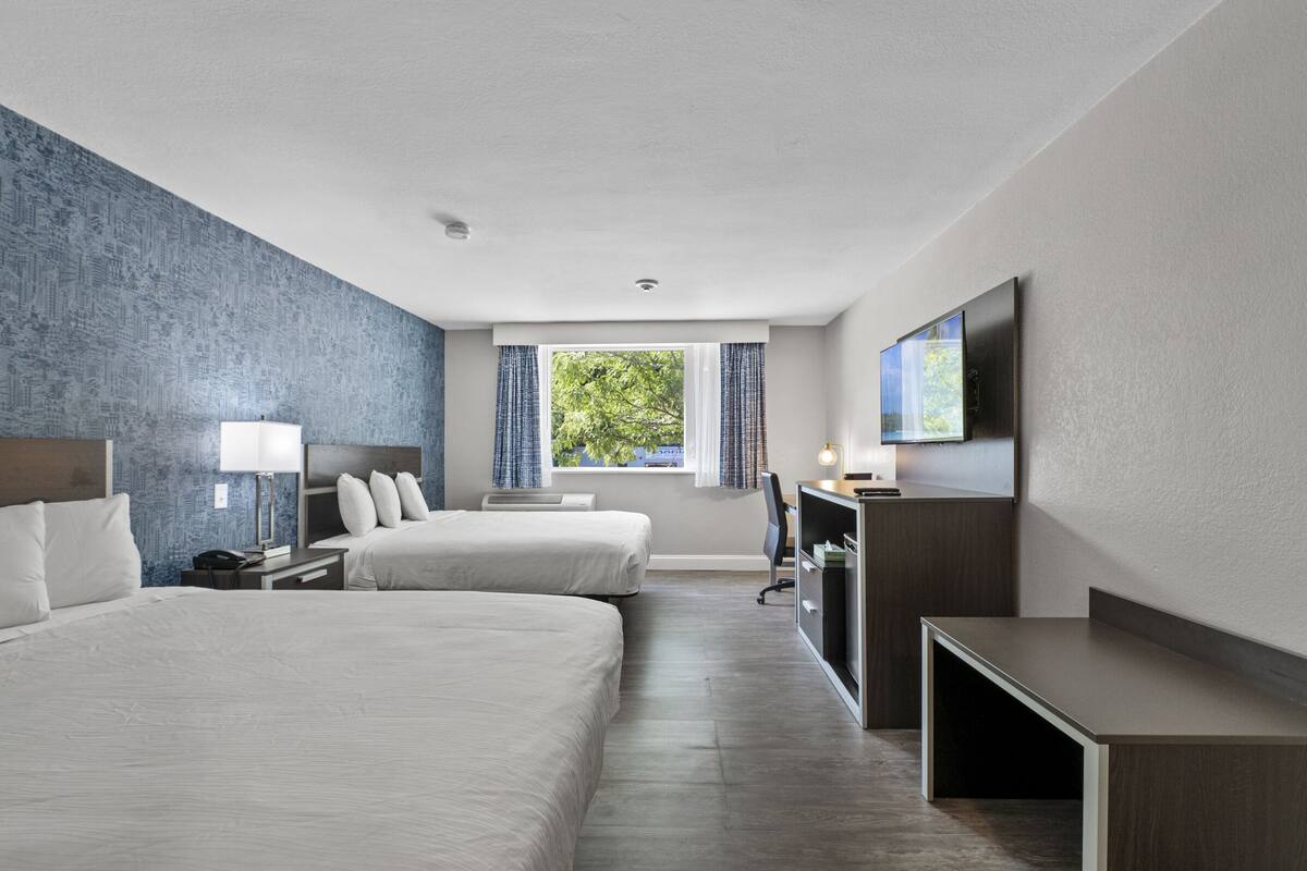 A hotel room with two beds, a desk, a TV, and a window with curtains.