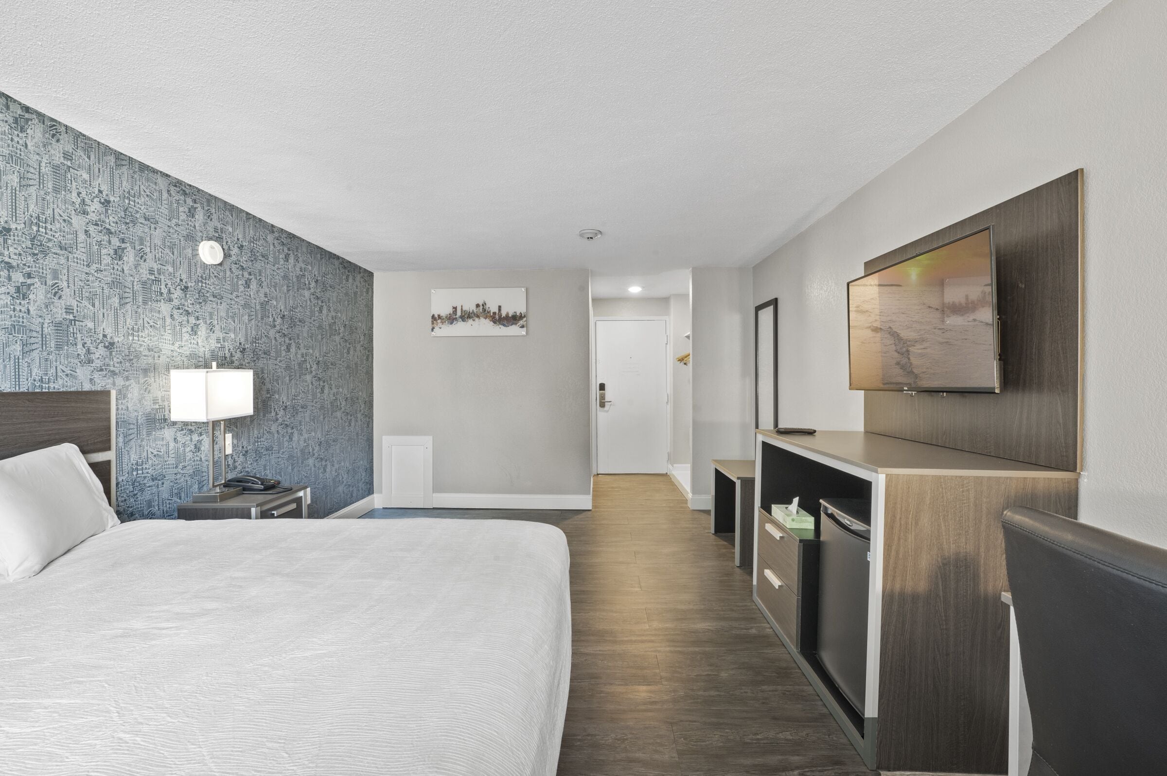 Habitación de hotel con una cama grande, un escritorio con silla, un televisor montado en la pared y una obra de arte con vista a la ciudad.