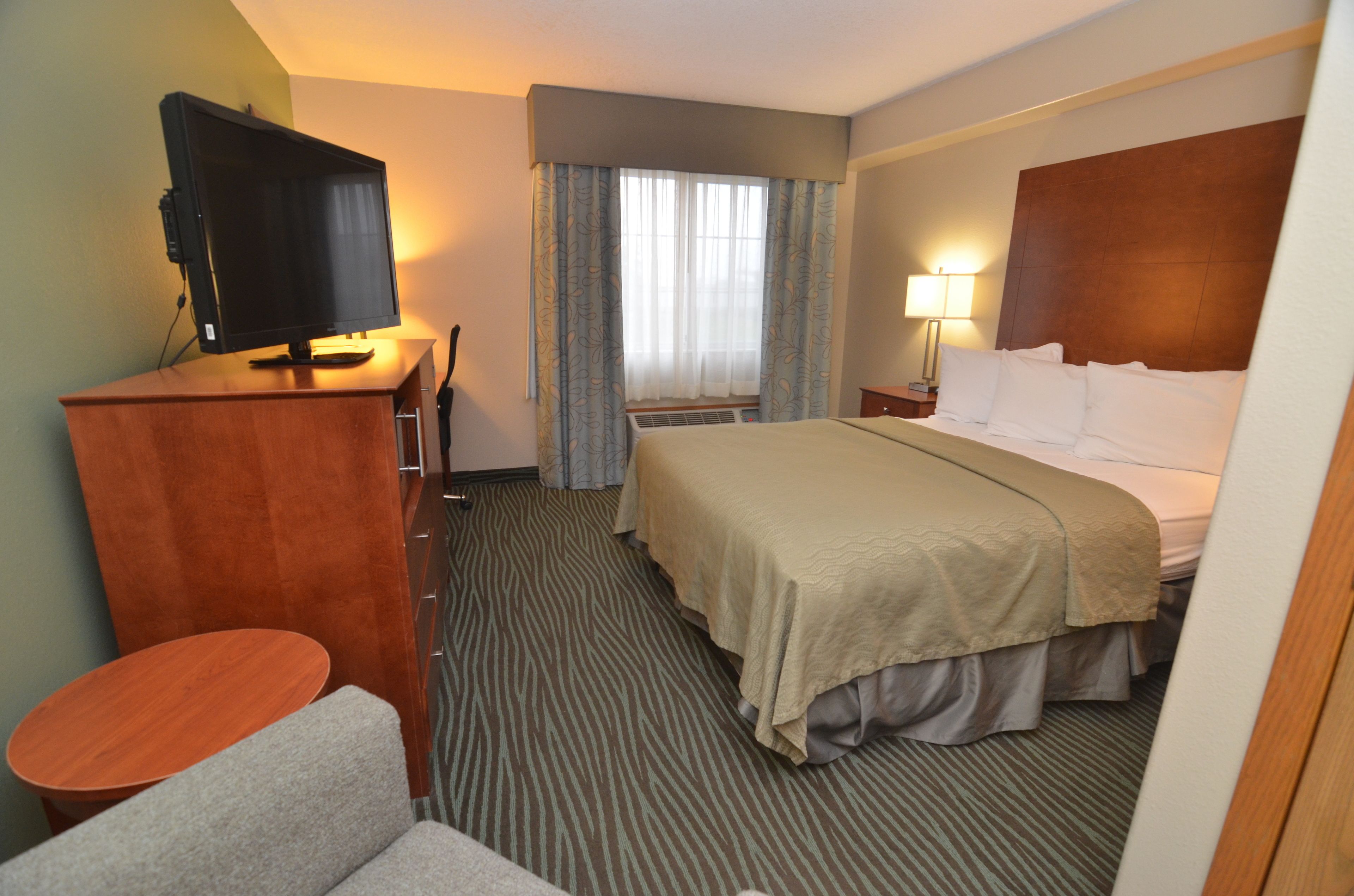 Ein Hotelzimmer mit Bett, Schreibtisch mit Fernseher, Stuhl, kleinem Tisch und einem Fenster mit Vorhängen.