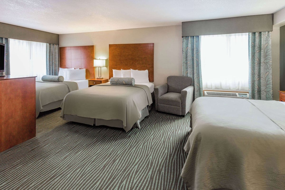 A hotel room with two beds, a desk, a chair, a TV, and a window with curtains.