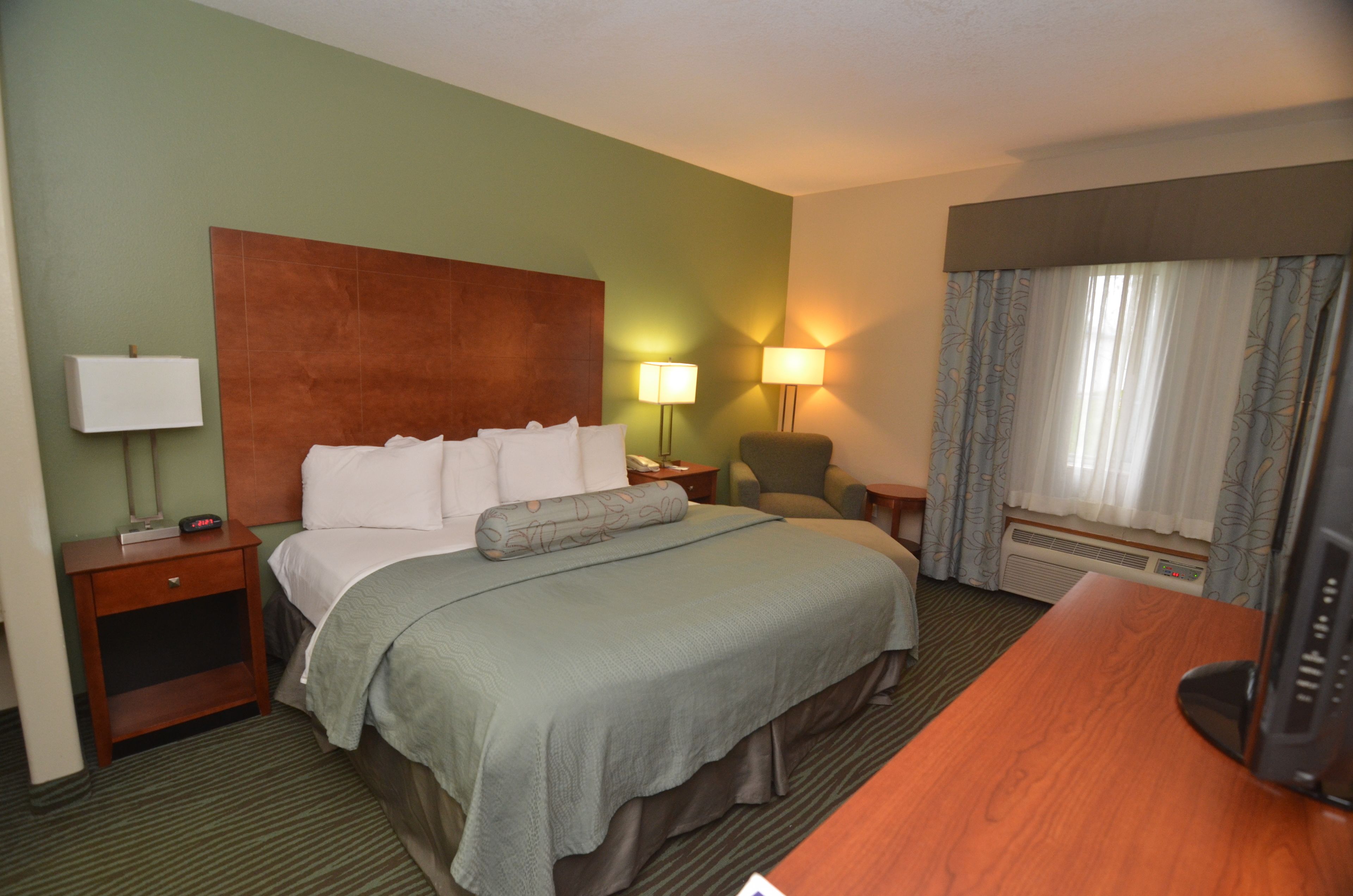 A hotel room with a bed, bedside tables, a desk, a lamp, and a television.