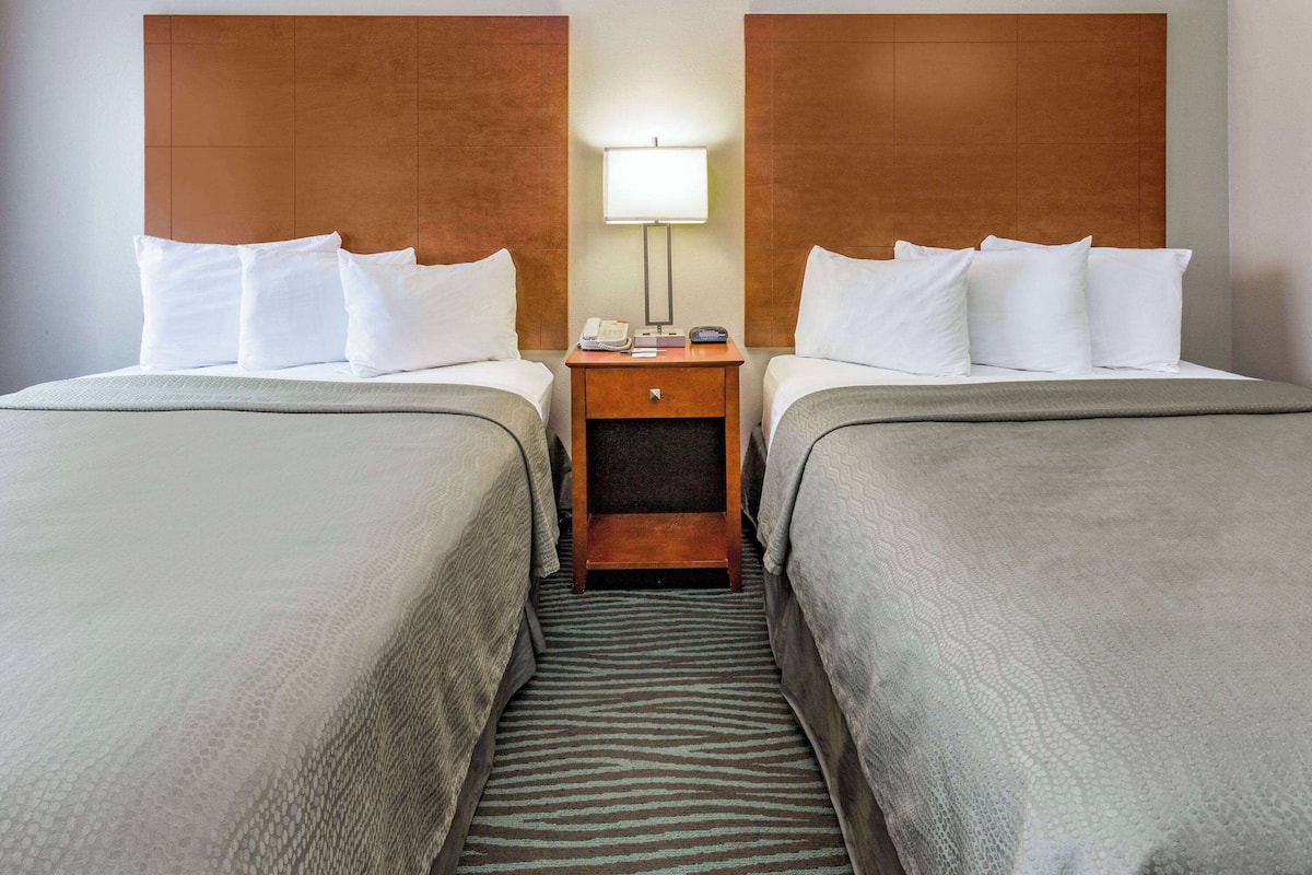 A hotel room with two beds, a nightstand with a lamp, a telephone, and a small table.