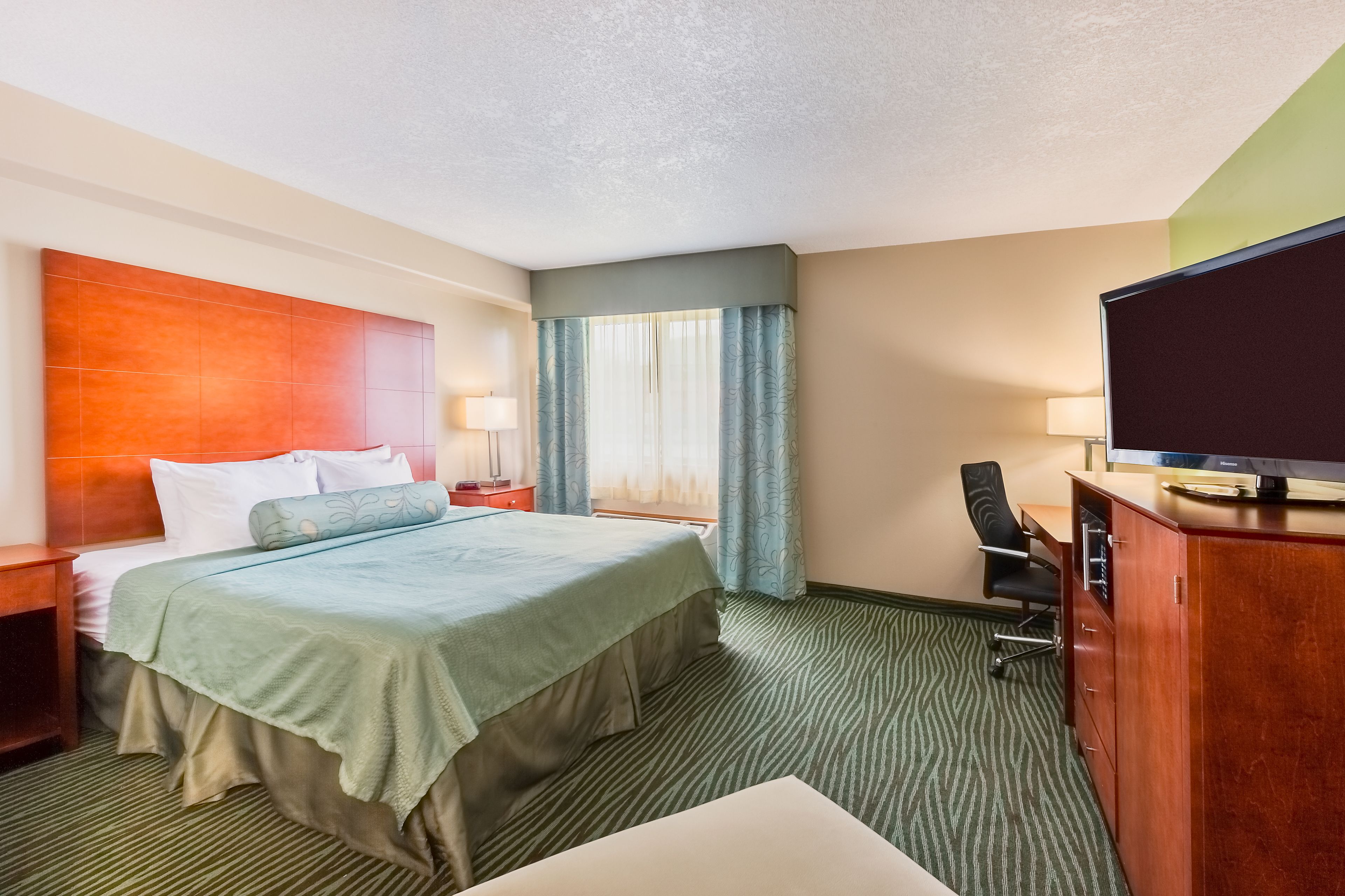 A hotel room with a bed, a desk, a television, and a window with curtains.