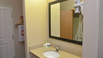 Un baño con lavamanos, espejo y secamanos.