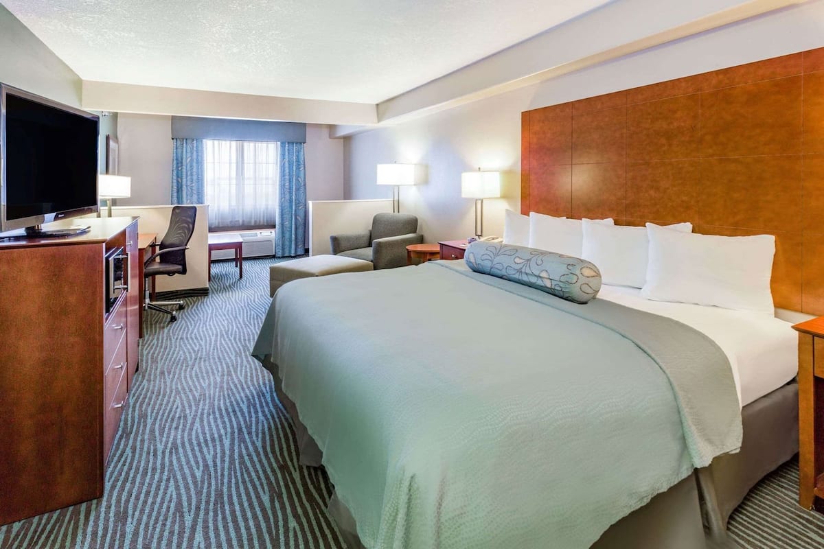 A hotel room with a large bed, a desk with a computer, a chair, a TV, and a window with curtains.