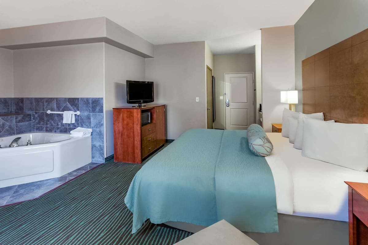 A hotel room with a large bed, a separate bathroom with a bathtub, a television on a wooden cabinet, and a door leading to another room.