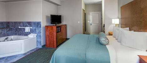 A hotel room with a large bed, a separate bathroom with a bathtub, a television on a wooden cabinet, and a door leading to another room.