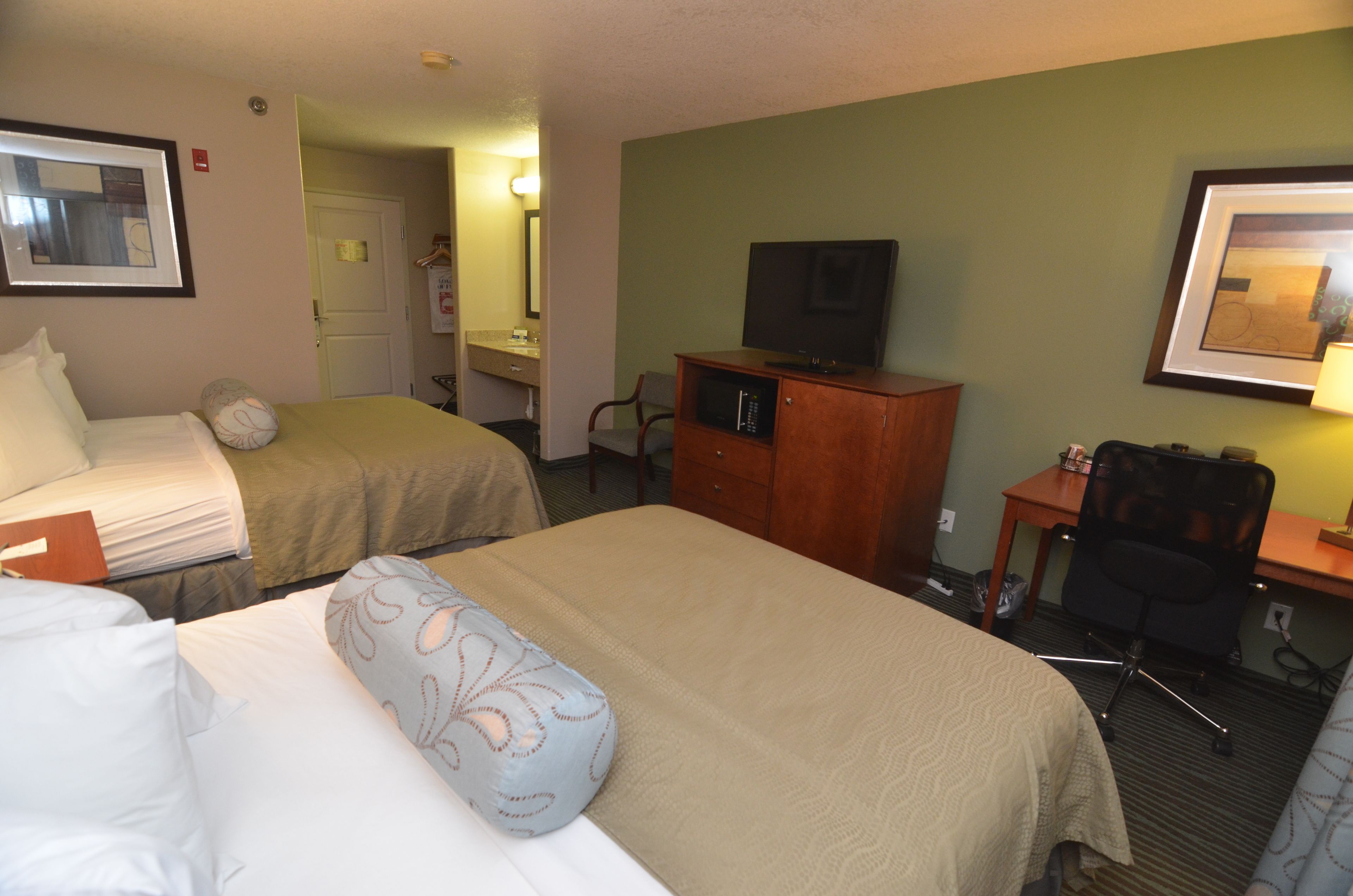 A hotel room with two beds, a desk with a chair, a television, and a framed picture on the wall.