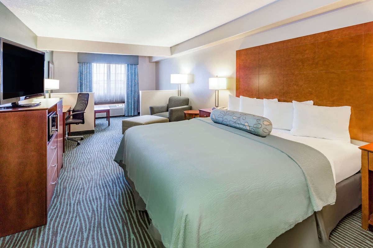 A hotel room with a large bed, a desk with a television, a chair, and two lamps.