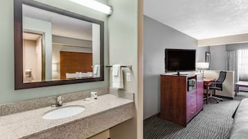 Une chambre d’hôtel équipée d’un lavabo avec un plan de travail en granit, d’un grand miroir, d’une télévision, d’un bureau et d’une chaise.