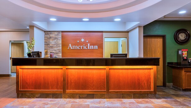 Een receptiebalie met een bord waarop 'AmericInn' staat en een klok aan de muur.