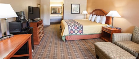 Quarto de hotel com cama, escrivaninha, televisão, cafeteira e sofá.