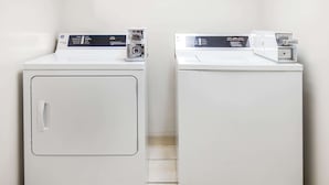 Two white front-loading washing machines side by side in a corner with tiled flooring. - Super 8 by Wyndham Clinton (Clinton)