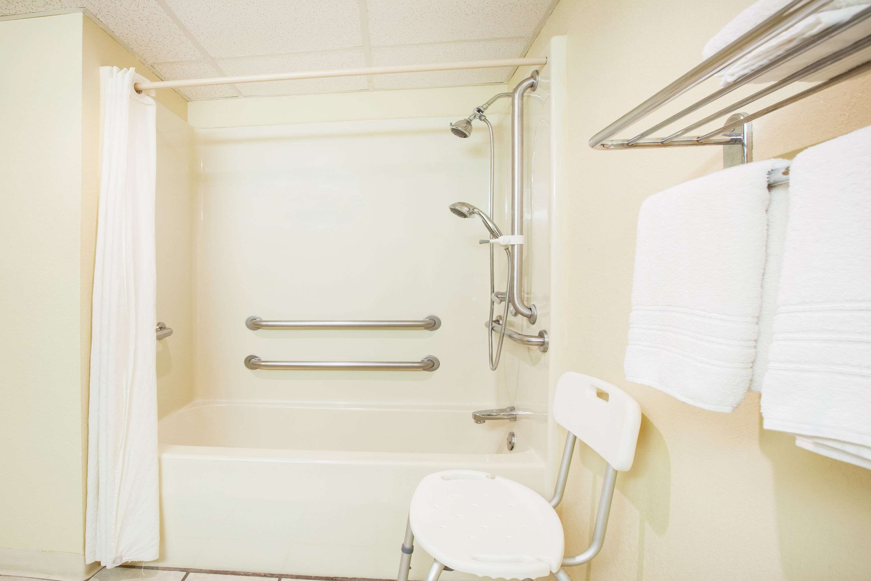Un baño con bañera, barras de apoyo, inodoro blanco y toallero.