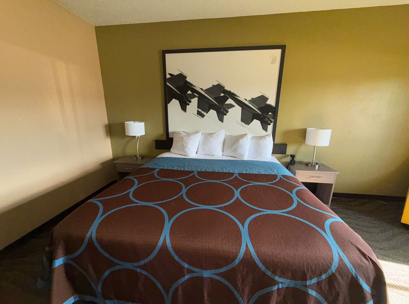 A hotel room with a bed, two bedside tables, a wall-mounted artwork, and a lamp on each table.