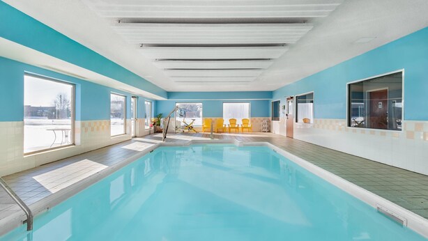 Una piscina interior con agua azul cristalina, sillas amarillas y vistas al exterior.
