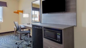 Habitación de hotel con televisión de pantalla plana montada en la pared, un escritorio con una silla, microondas y refrigerador.