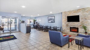 Un hall de hotel con pared de piedra, chimenea y zona de estar con sofás y mesas.