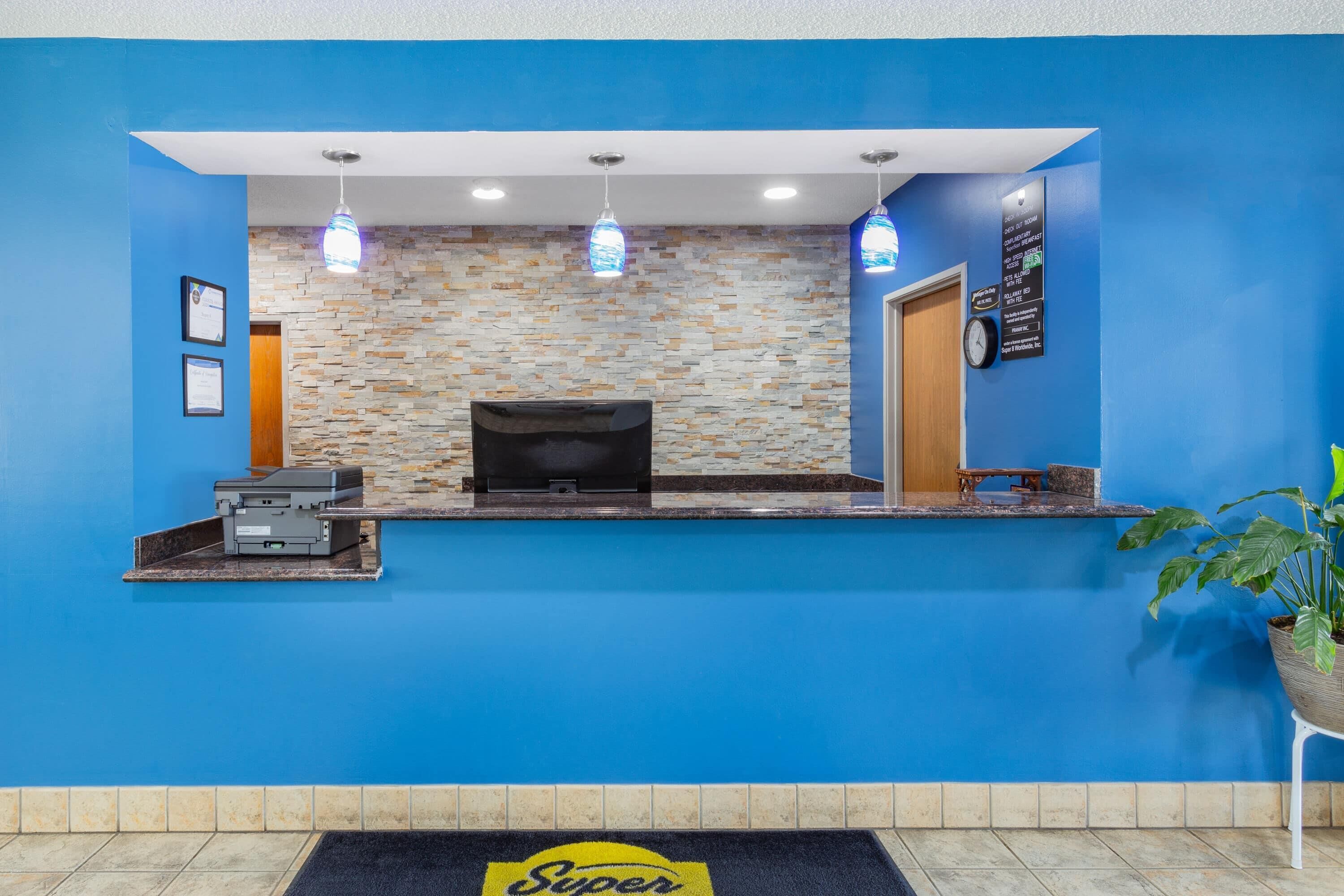 Zona de recepción con pared azul, fondo con diseño de piedra y mostrador de recepción con televisor de pantalla plana.