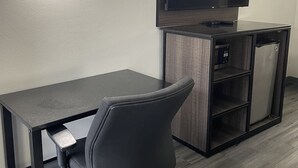 A modern hotel room with a flat-screen TV mounted on the wall, a dark wooden desk, and a black office chair. - Griffin Inn and Suites (Griffin)