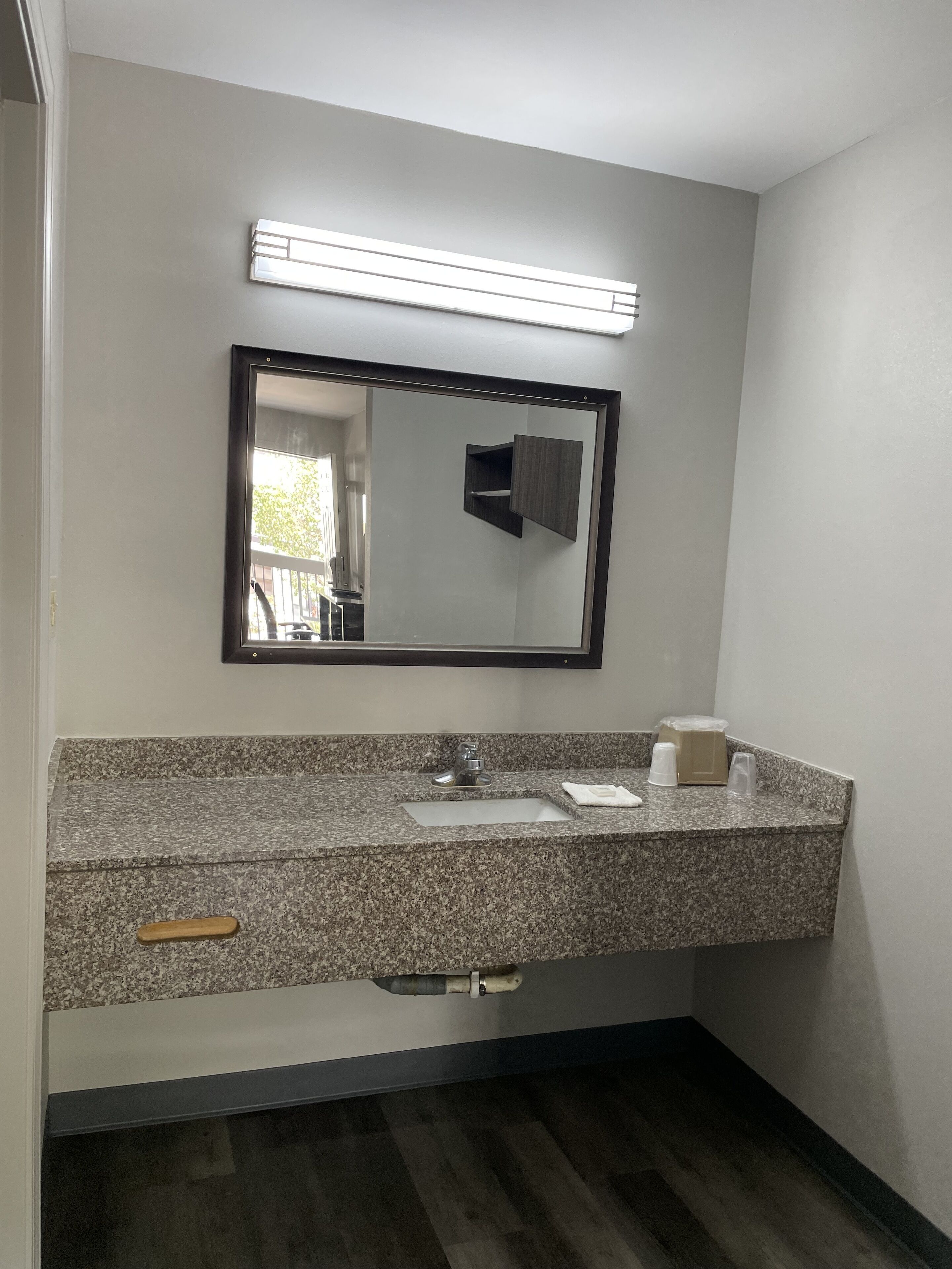 A bathroom with a granite countertop, a sink, a mirror, and a wooden handle drawer.