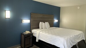 A hotel room with a large bed, a bedside table with a phone, and wall-mounted lights. - Griffin Inn and Suites (Griffin)