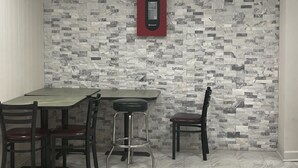 A dining area with a marble floor, a table with four chairs, and a red emergency exit sign on the wall. - Griffin Inn and Suites (Griffin)