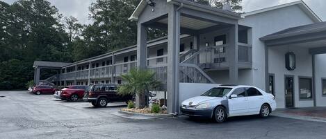 A motel with a covered parking area, a palm tree, and a staircase leading to the entrance.