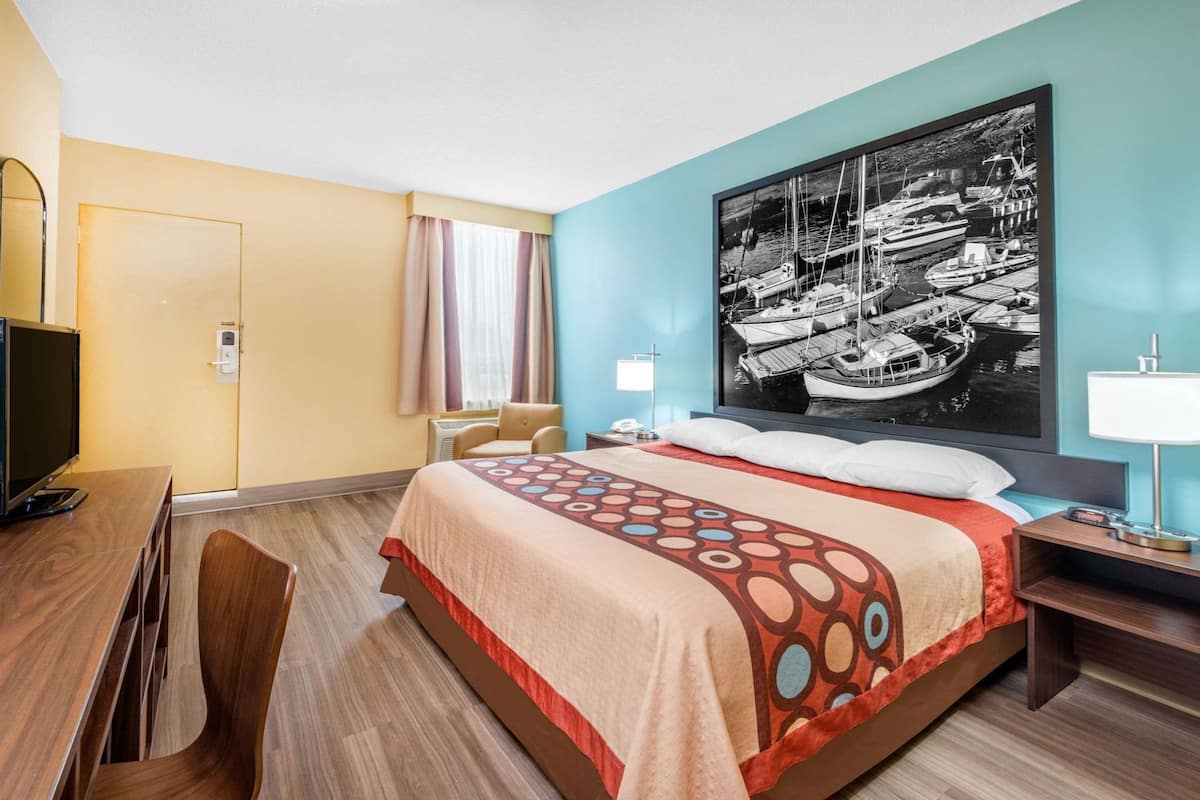 Une chambre d’hôtel avec un lit, un bureau, une chaise, une télévision et une grande fenêtre.