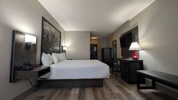 A hotel room with a large bed, a desk with a lamp, a TV, and a bench.
